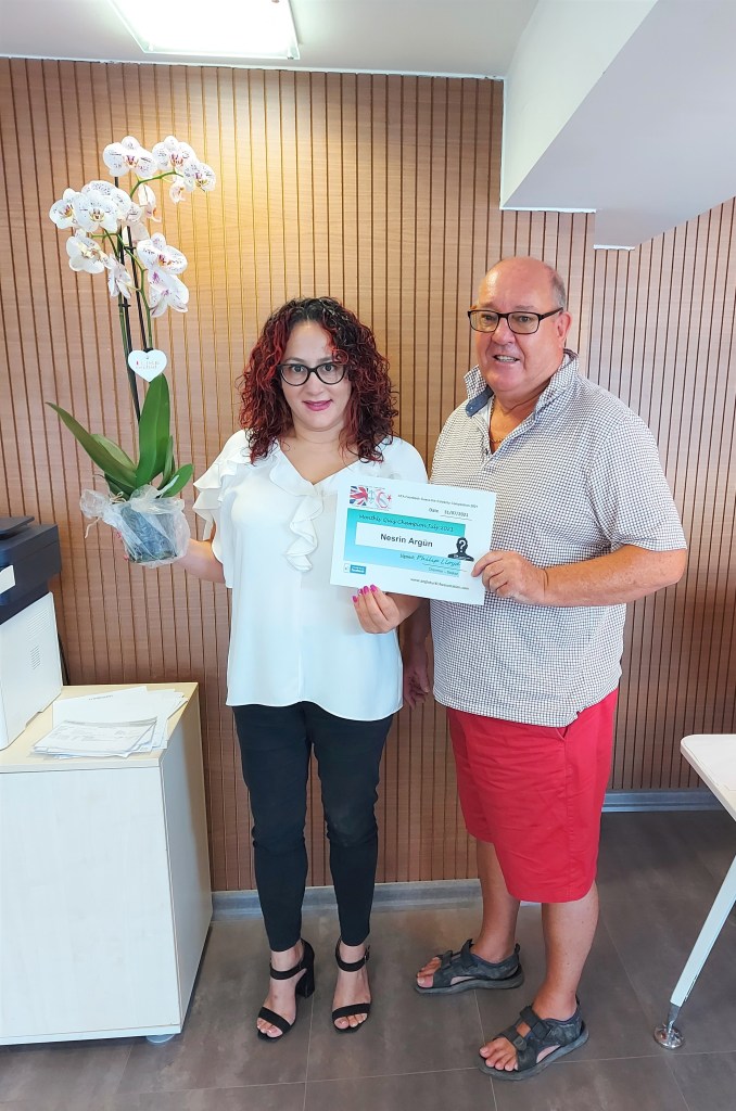JULY 2021 Monthly prize winner (person with the most correct guesses during the month) is: - Nesrin Argün seen here receiving her prize and certificate from the association chairman