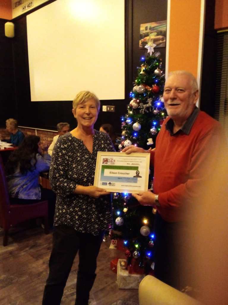 NOVEMBER 2023 Monthly prize winner (person with the most correct guesses during the month) is: –  Eileen Croucher (L) seen here receiving her winners certificate from the associations Richard Currie